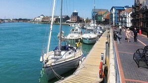 A marina with boats docked along a wooden pier, a pedestrian walkway, and buildings in the background. - Spacious Seafront Apartment, Garden & Free Parking (Littlehampton)