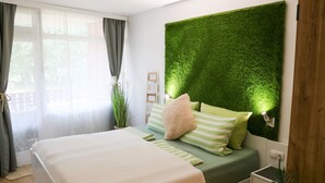 Ein Schlafzimmer mit einem Bett, grüner Bettwäsche, einer grünen Wand, einem Nachttisch und einer Topfpflanze.