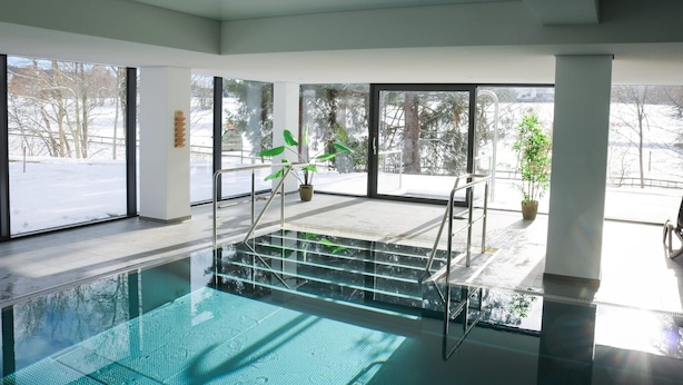 Ein Innenpool mit Glaswänden, Stufen zum Pool und Kübelpflanzen.