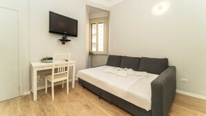 Een slaapkamer met een bed, een bureau, een stoel, een aan de muur bevestigde televisie en een raam.