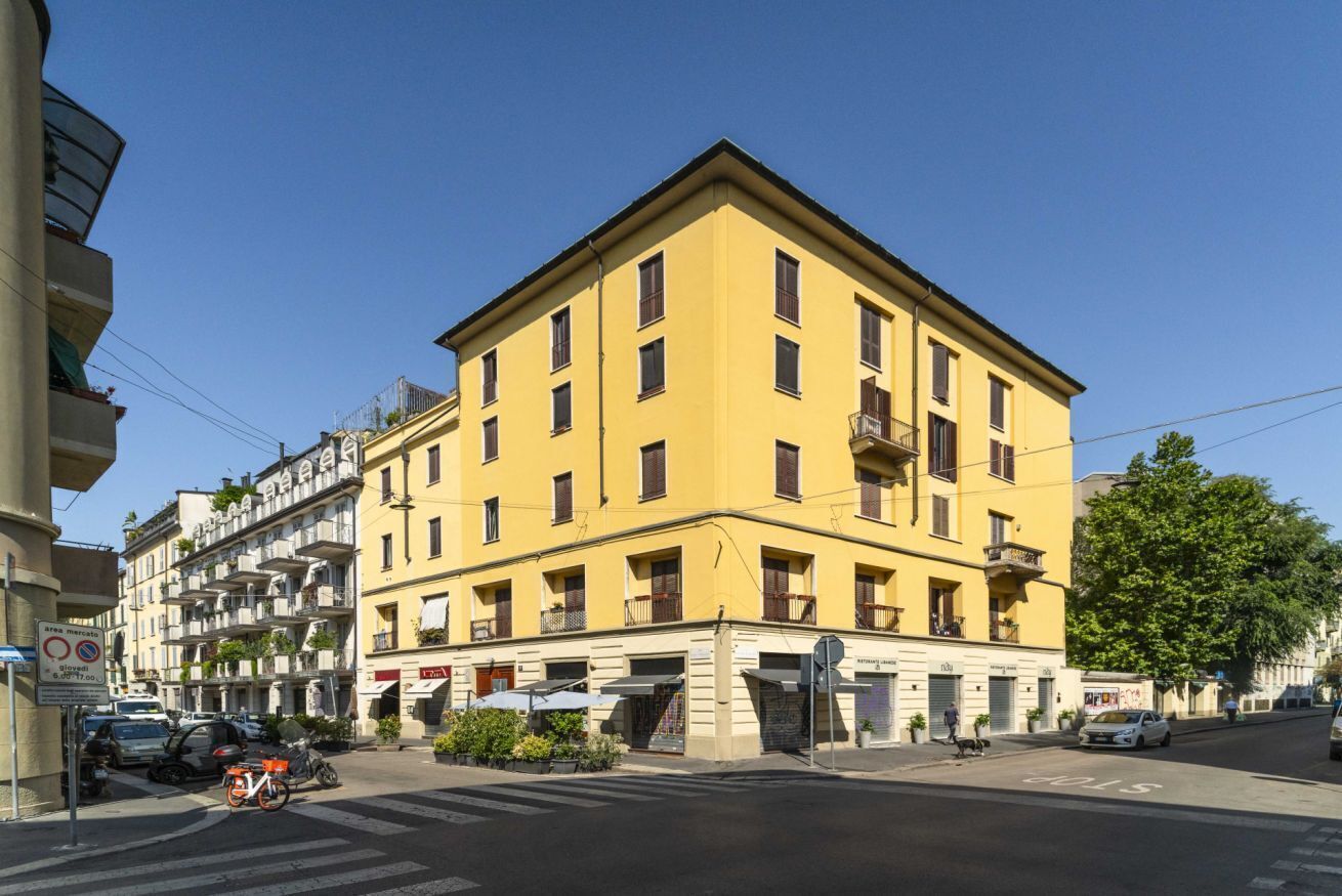 A yellow building with multiple floors, balconies, and a ground-level entrance.