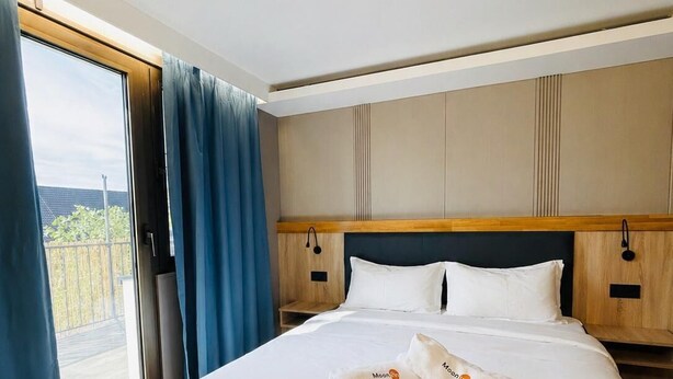 A hotel room with a large bed, wooden headboard, and a view through a large window. - Mooncity Hotel & Boardinghouse  (Düsseldorf)