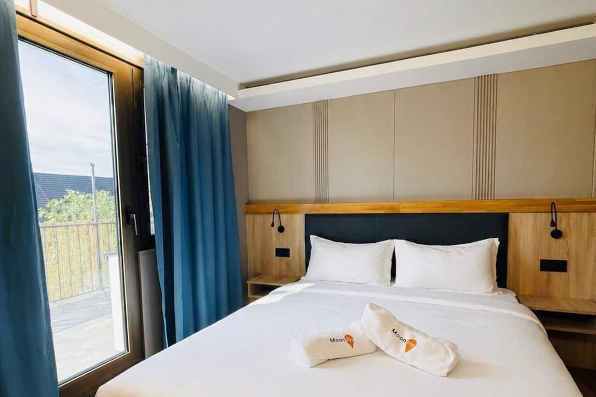 Une chambre d’hôtel avec un grand lit, une tête de lit en bois et une vue dégagée sur l’extérieur grâce à une grande fenêtre.