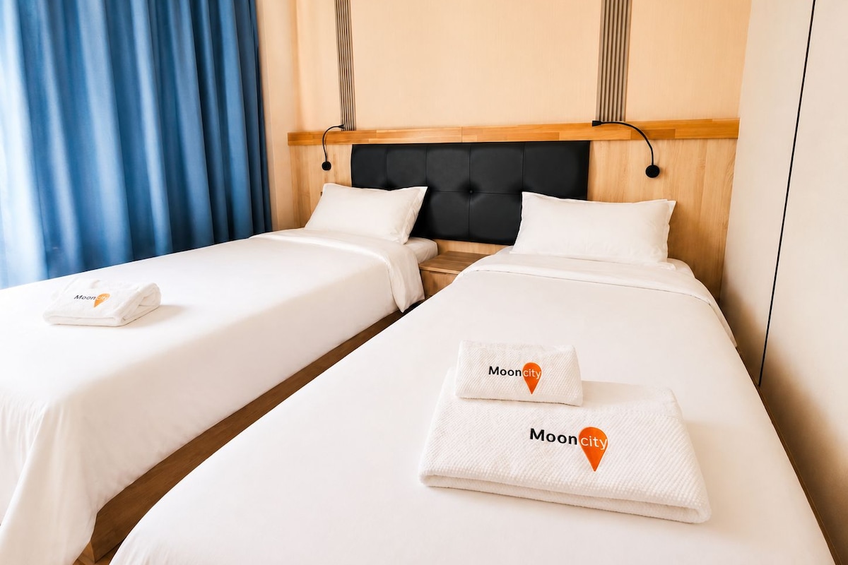 Habitación de hotel con dos camas, cabecero de madera y cortina azul.