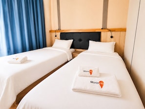Habitación de hotel con dos camas, cabecero de madera y cortina azul.