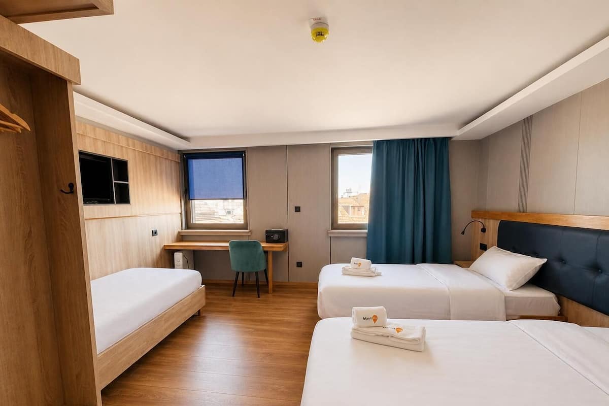 Une chambre d’hôtel avec deux lits, un bureau, une chaise et une fenêtre avec des rideaux.