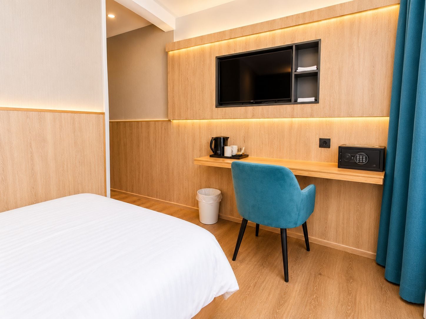 A hotel room with a bed, a desk with a chair, a television, a coffee maker, and a trash bin.