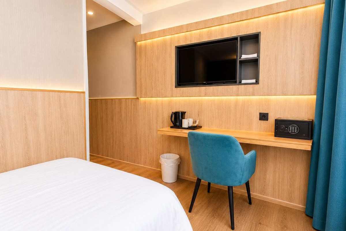 Habitación de hotel con cama, escritorio con silla, televisor, cafetera y basurero.