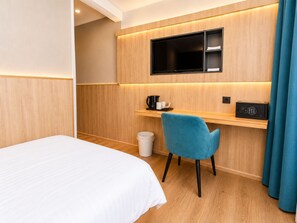 A hotel room with a bed, a desk with a chair, a television, a coffee maker, and a trash bin. - Mooncity Hotel & Boardinghouse  (Düsseldorf)