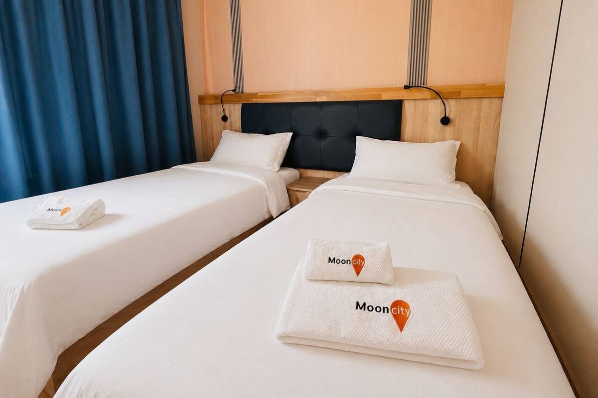 Une chambre d’hôtel avec deux lits simples, une tête de lit en bois et un rideau bleu.