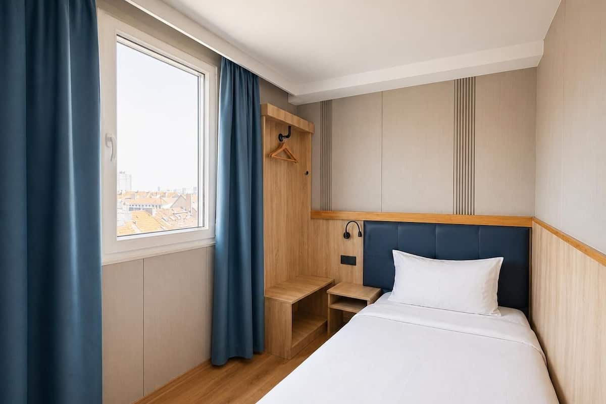 Une chambre d’hôtel avec un lit, une table de chevet, un porte-manteau et une fenêtre avec des rideaux.