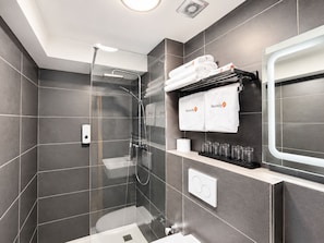 A modern bathroom with a glass-enclosed shower, a toilet, and a sink. There are towels and toiletries on a shelf. - Mooncity Hotel & Boardinghouse  (Düsseldorf)