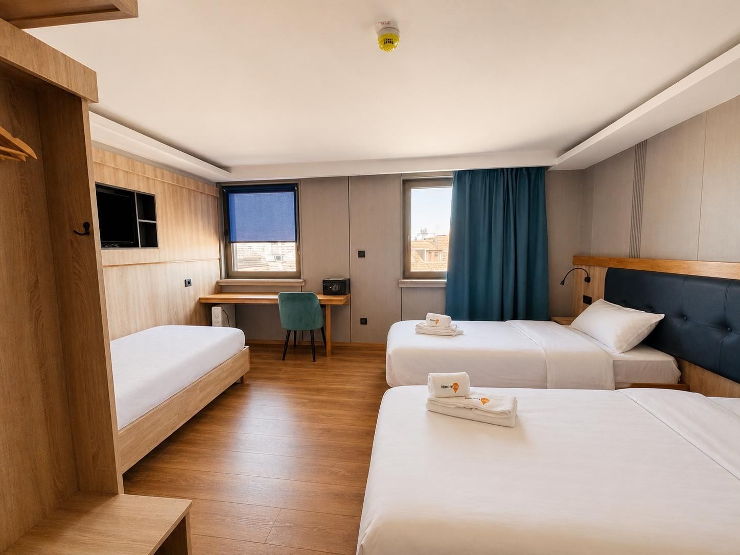 Habitación de hotel con dos camas, un escritorio, una silla y una ventana con cortinas.