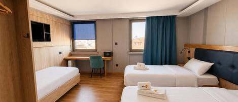 Una camera d'albergo con due letti, una scrivania, una sedia e una finestra con tende.