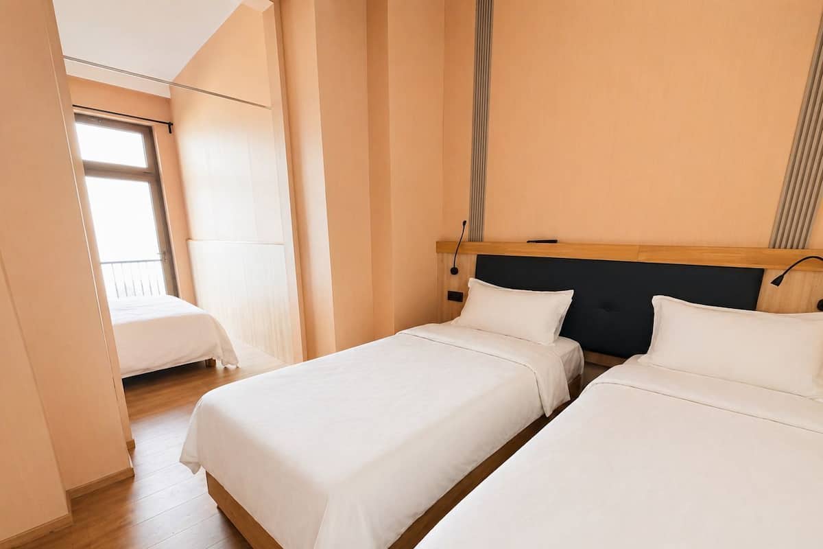 Une chambre d’hôtel avec deux lits, une tête de lit en bois, une fenêtre et un balcon.