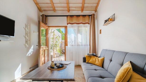 A living room with a sofa, a coffee table, a flat-screen TV, and a window with curtains. - Studio "Maya" with Private Terrace, Shared Garden, and Wi-Fi (Le Puy-Sainte-Réparade)