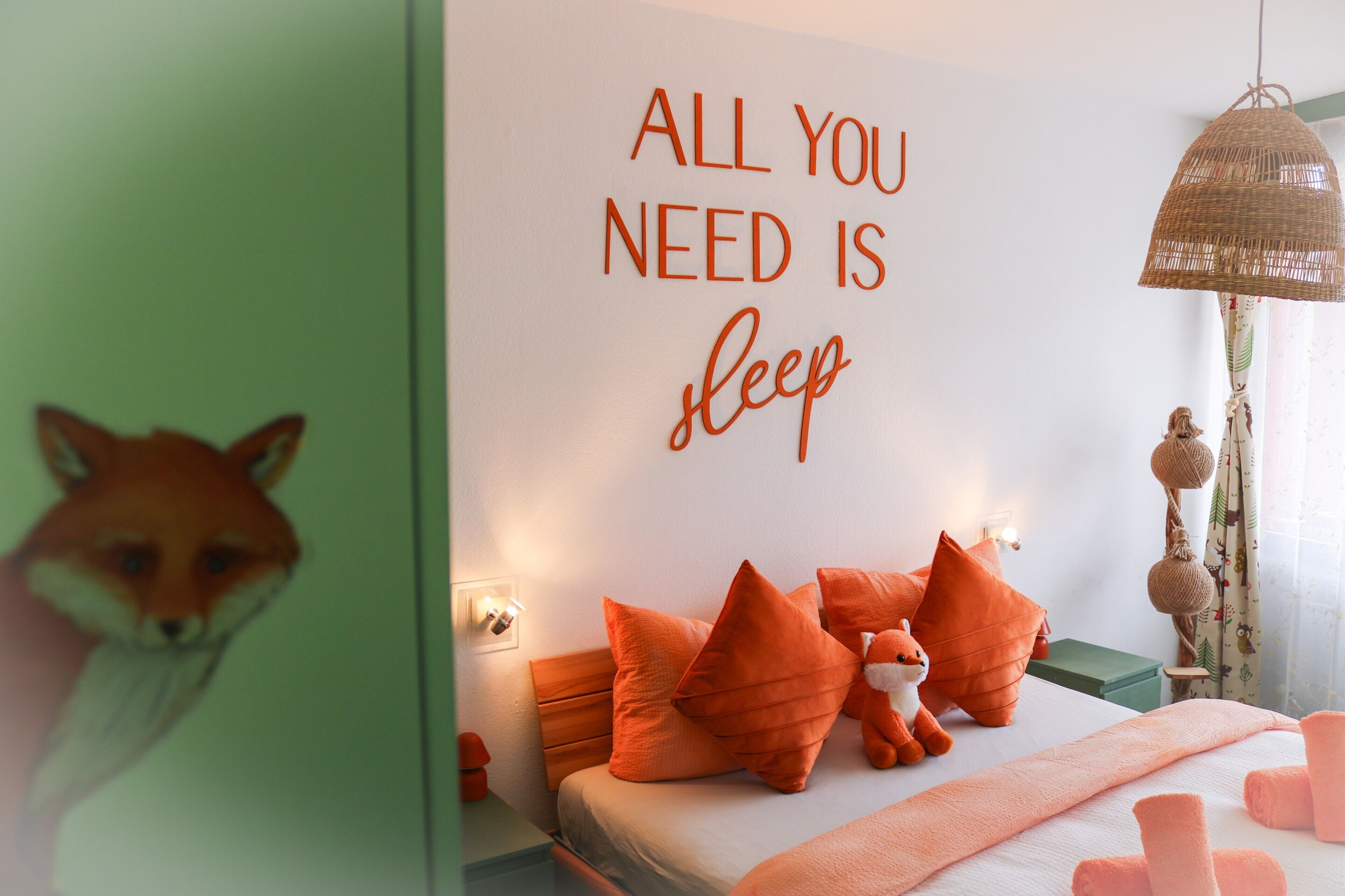 Ein Schlafzimmer mit einem Bett, orangefarbenen Kissen, einem Fuchs-Plüschtier und einem Schild an der Wand mit der Aufschrift 'ALL YOU NEED IS sleep'.