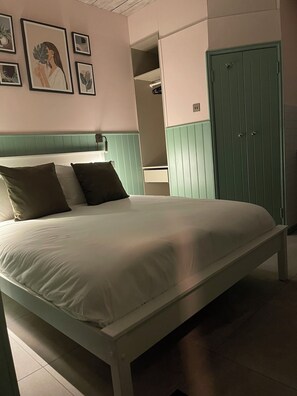 Una cama con colchón blanco y dos almohadas, cabecera verde y un armario verde con dos puertas.