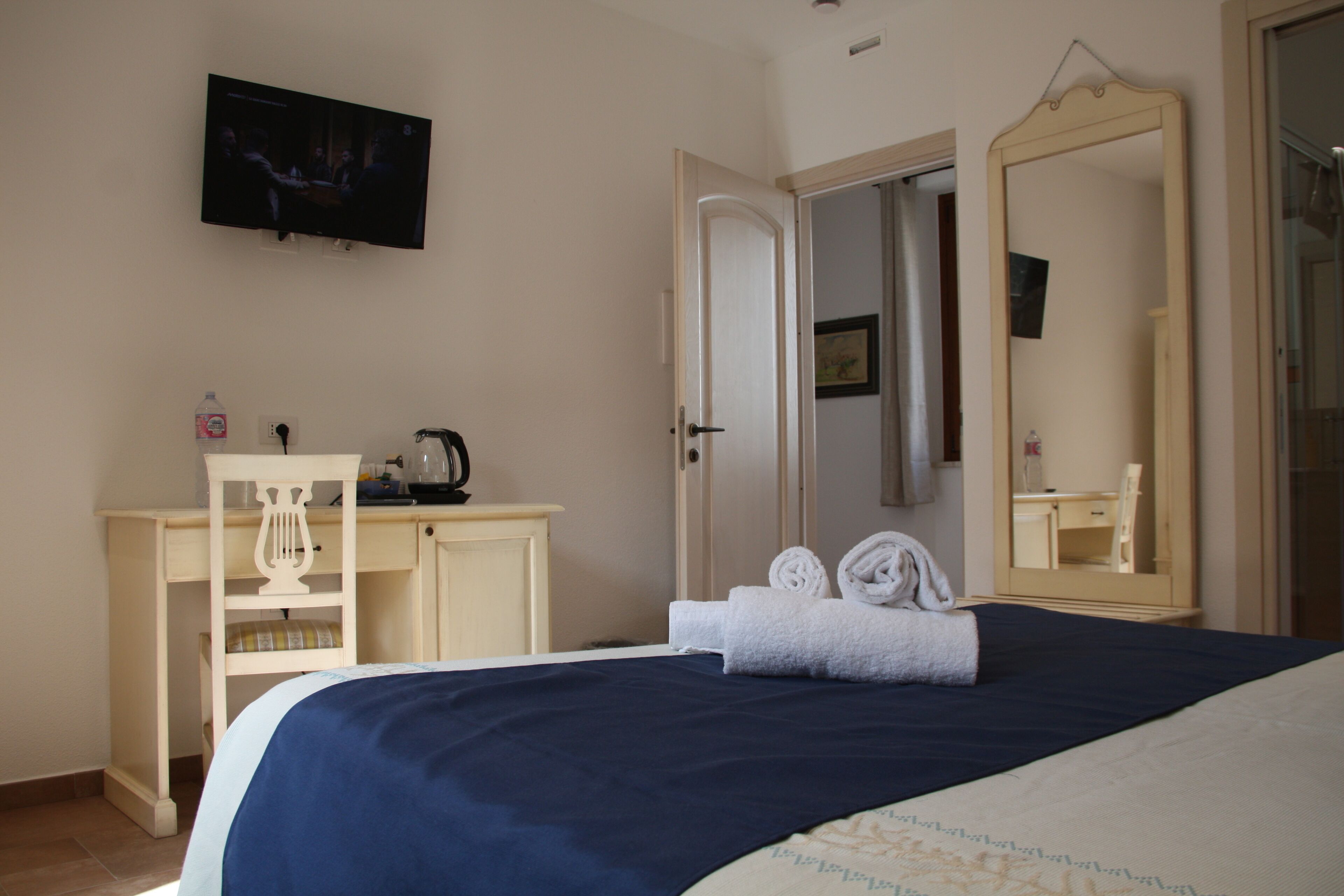 A bedroom with a bed, a desk, a chair, a television, a mirror, and a door.