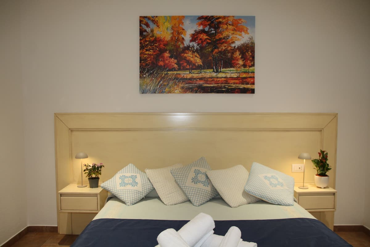 A neatly made bed with a blue and white color scheme, flanked by two bedside tables with lamps and potted plants.