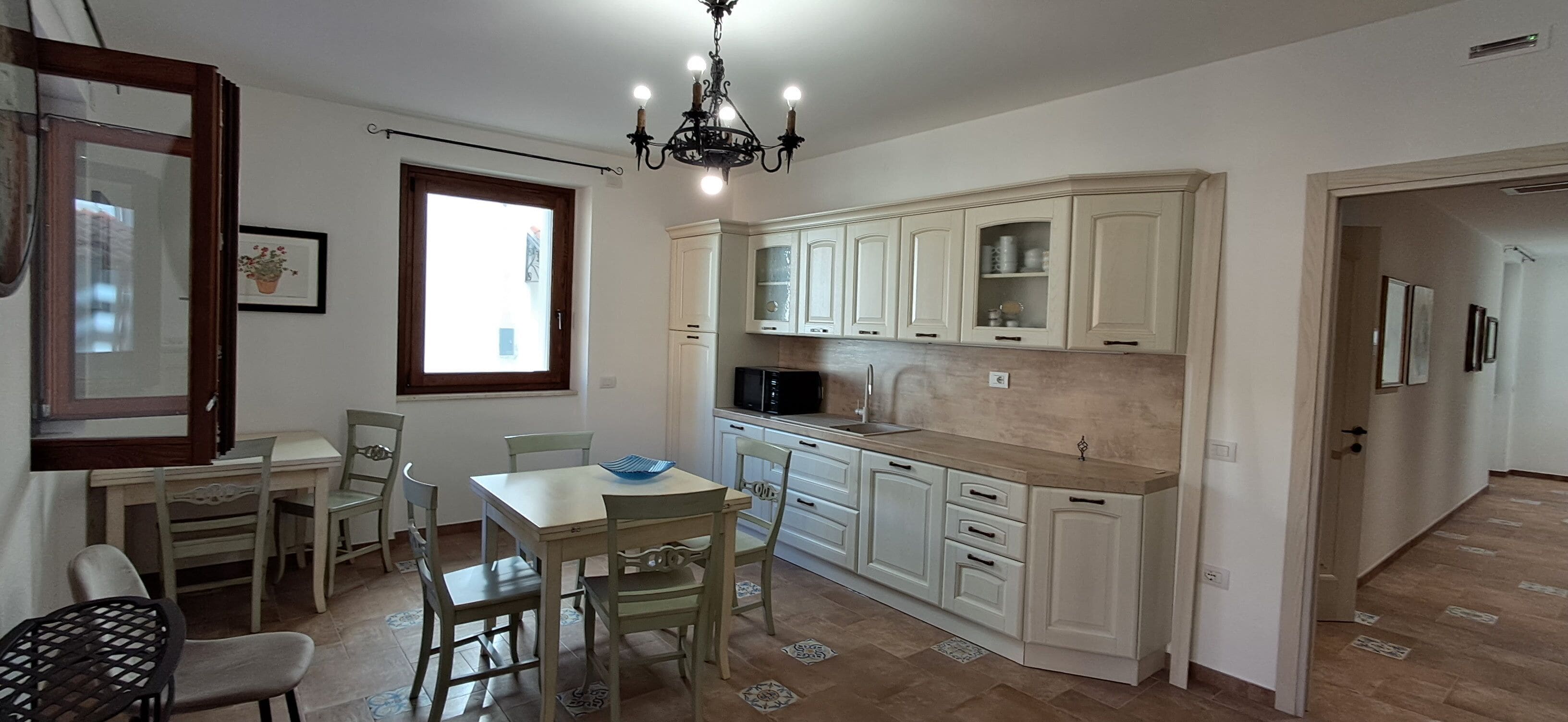 A kitchen with white cabinets, a dining table with chairs, a chandelier, and a window.