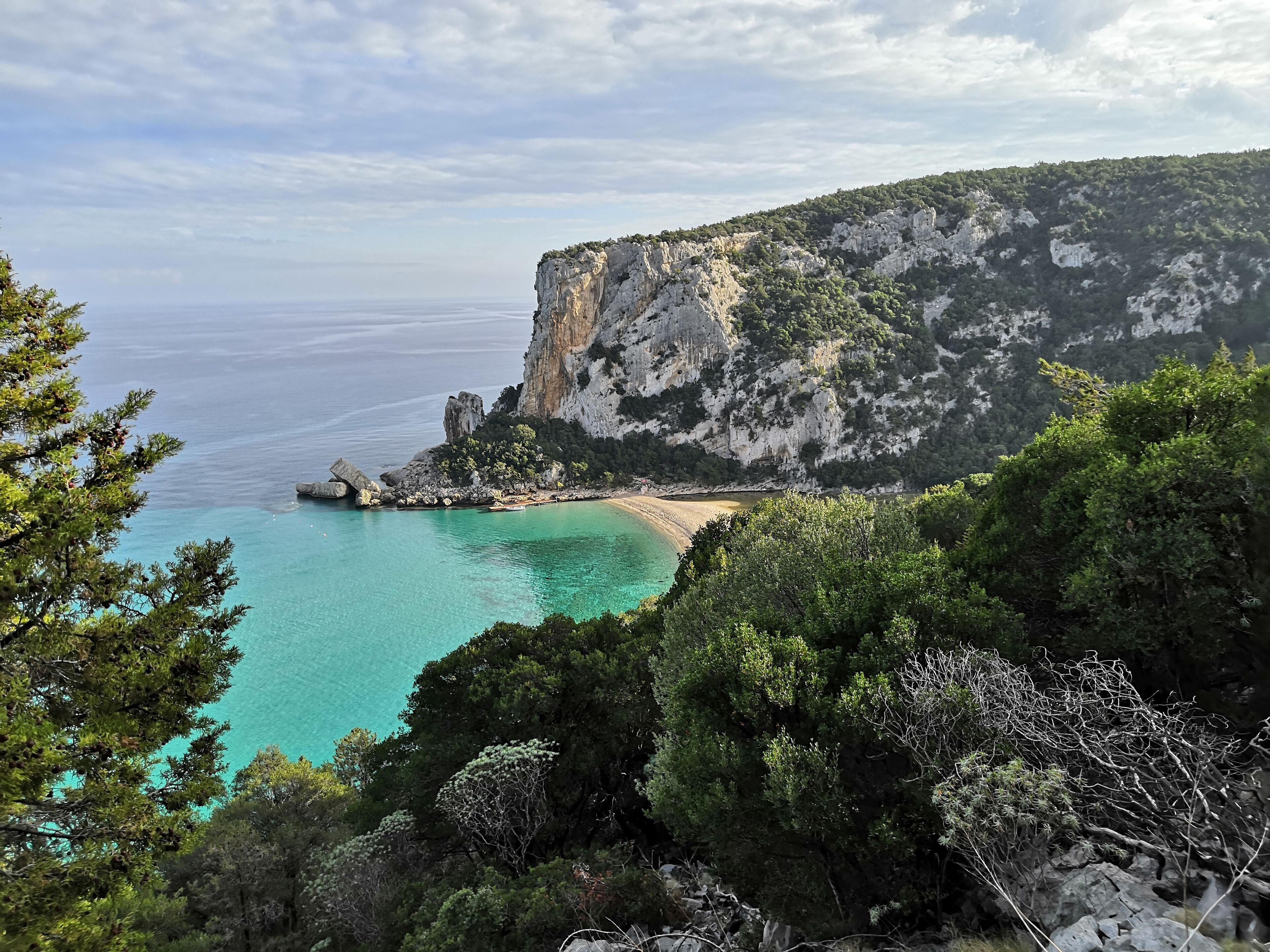 A coastal landscape with a clear turquoise sea, a sandy beach, and rocky cliffs.