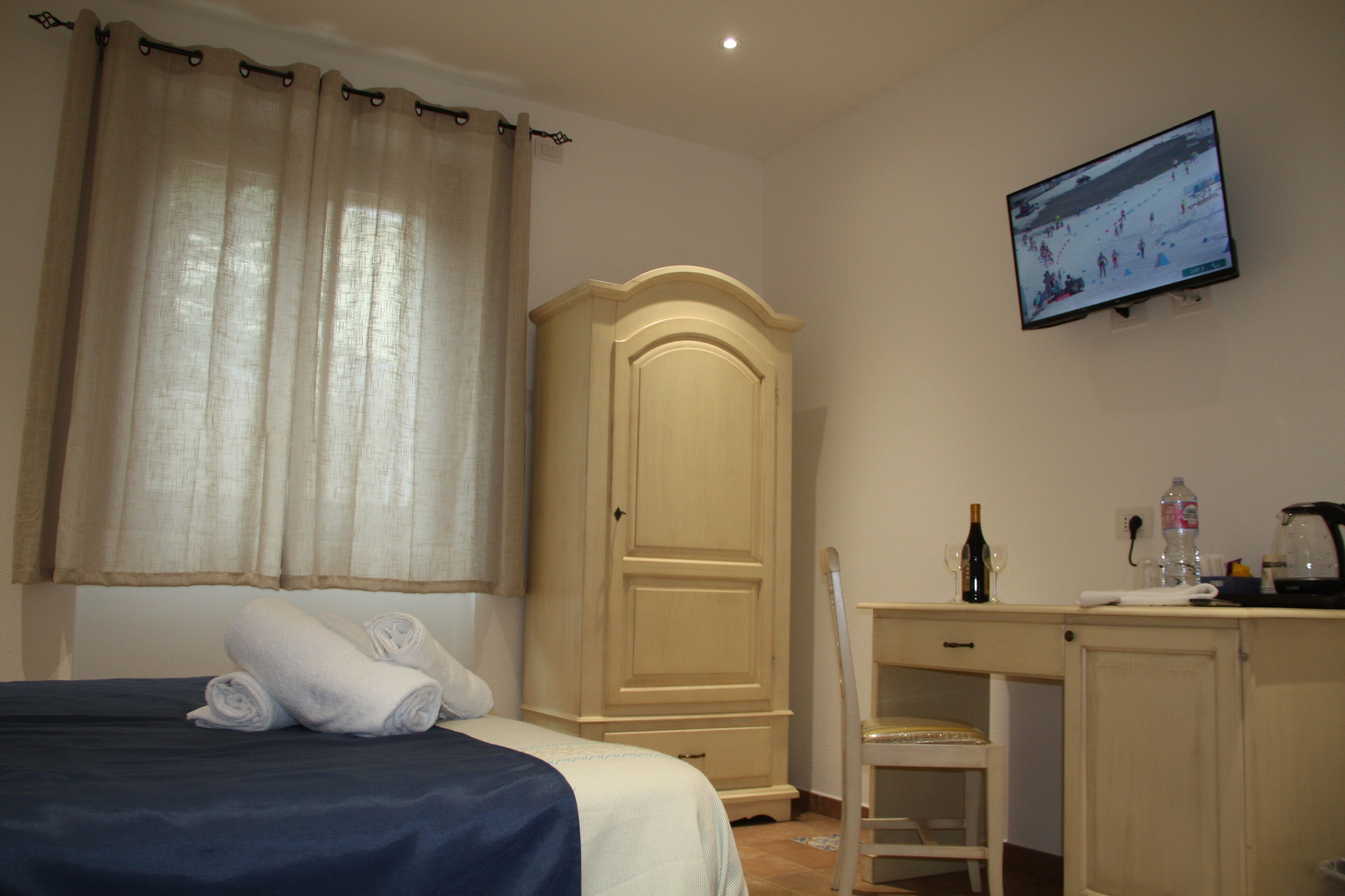 Habitación de hotel con cama, armario, escritorio con silla y televisor montado en la pared.