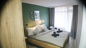 A bedroom with a wooden bed, white bedding, a green wall, and a window with curtains. - "Schönhier" – Designer Apartment with Pool, Sauna & More (Schluchsee)