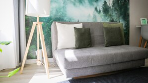 A grey sofa with two cushions, a floor lamp, and a forest-themed wall mural. - "Schönhier" – Designer Apartment with Pool, Sauna & More (Schluchsee)