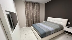 A modern bedroom with a bed, curtains, a nightstand, and a TV mounted on the wall. - Turin Urban Marble Suite (TORINO)