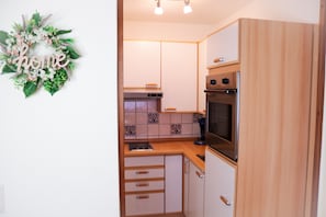 A kitchen with wooden cabinets, a stove, and a microwave. - "Morgensonne" – Pool, Sauna & Relaxation (Schluchsee)