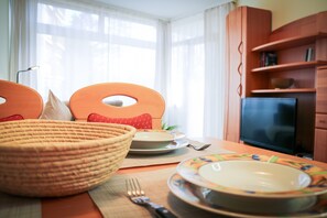A dining area with a table set for two, a wicker basket, a television, and a bookshelf. - "Morgensonne" – Pool, Sauna & Relaxation (Schluchsee)