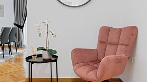 A modern room with a round mirror, a pink chair, a small table with a plant, and a herringbone wooden floor. - Kolonaki Luxury Residence, Bill & John Apartments & Villas (Athens)
