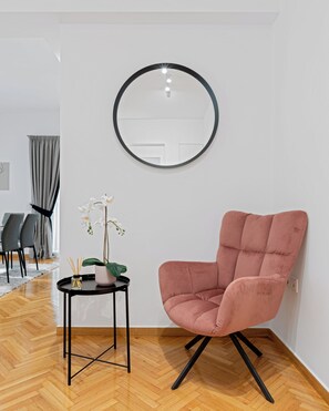 A modern room with a round mirror, a pink chair, a small table with a plant, and a herringbone wooden floor. - Kolonaki Luxury Residence, Bill & John Apartments & Villas (Athens)