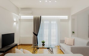 A modern living room with a flat-screen TV, a glass coffee table, a sofa, and a large window with sheer curtains. - Kolonaki Luxury Residence, Bill & John Apartments & Villas (Athens)