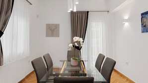 A modern dining area with a glass table, grey upholstered chairs, and a vase with white orchids. - Kolonaki Luxury Residence, Bill & John Apartments & Villas (Athens)