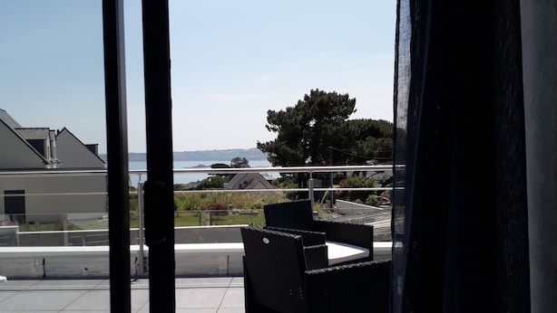 En balkon med et bord og stole, der ud til et vandområde og fjerne bygninger.
