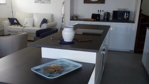 Et moderne køkken med en central ø, et spiseområde med barstole, en sofa og et ur på væggen.