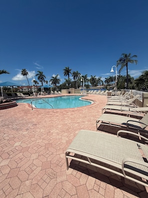 A pool area with hexagonal tiles, lounge chairs, and palm trees.