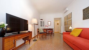 A living room with a television, a sofa, a dining table with chairs, and a red couch. - Riboty House al Vaticano (Roma)