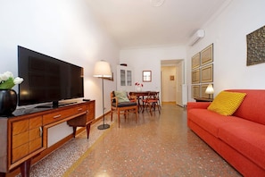 A living room with a television, a sofa, a dining table with chairs, and a red couch. - Riboty House al Vaticano (Roma)