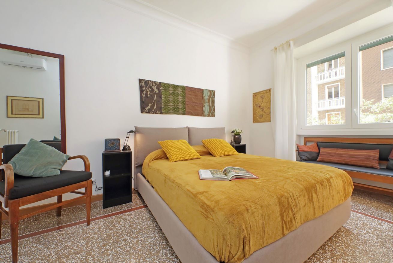 A bedroom with a bed, a chair, a nightstand, and a window.