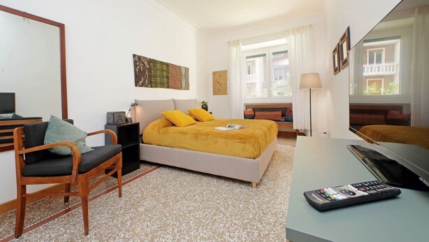 A hotel room with a bed, a desk, a chair, a TV, and a window with curtains. - Riboty House al Vaticano (Roma)