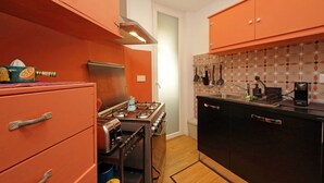 A compact kitchen with orange cabinets, a stove, and a sink. - Riboty House al Vaticano (Roma)