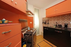 A compact kitchen with orange cabinets, a stove, and a sink. - Riboty House al Vaticano (Roma)