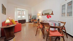 A cozy living room with a red sofa, a wooden dining table with chairs, a lamp, and a television. - Riboty House al Vaticano (Roma)