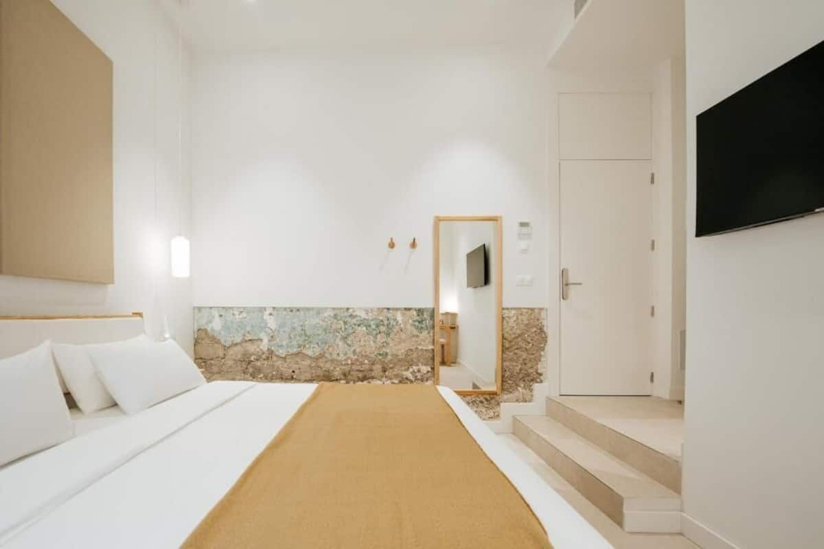 Une chambre d’hôtel avec un lit, un téléviseur fixé au mur et une porte donnant sur une autre pièce.