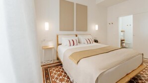 Una habitación de hotel moderna con una cama grande, una mesita de noche, un espejo y una alfombra con estampado geométrico.