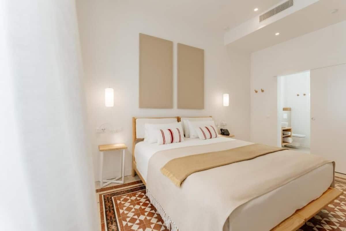 Une chambre d’hôtel moderne avec un grand lit, une table de chevet, un miroir et un tapis à motifs géométriques.