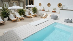 Zona junto a la piscina con sillones, sombrillas, plantas en macetas y un pequeño rincón de descanso.